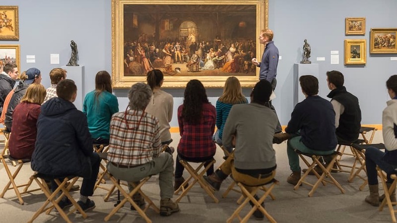 Group of people observing a painting while a faculty member lectures about it