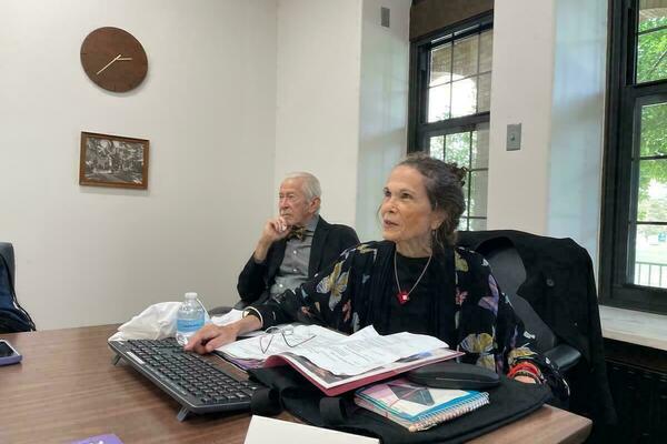 Author Julia Alvarez, in a colorful butterfly-patterned jacket and red necklace, with her husband in the background