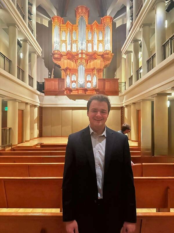 Smiling man in suit stands in Notre Dame's Reyes Organ and Choral Hall with its large, ornate Fritts pipe organ.