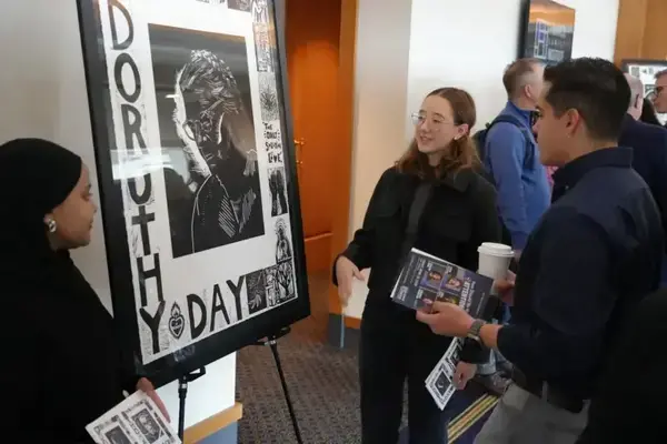 Students Rena Hassan, left, and Mayalen Fortoul Belausteguigoitia, middle, share portrait of Dorothy Day to attendee of the Dorothy Day & Thomas Merton Culture and the Public Good Symposium