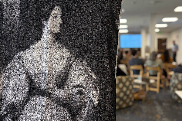 Weaving of a woman in a Victorian-era dress in the foreground with a group watching presentations in the background.